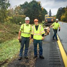 A seasoned AOT maintenance worker poses with a young intern on the roadside of a maintenance acitivity