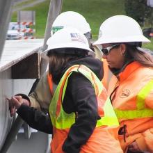 Three workers in hard hats point to a bridge beam